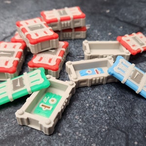 May include: A collection of small, gray, white, red, blue, and green plastic boxes with lids. Some of the boxes are open and show the inside of the boxes. The boxes have a variety of designs and patterns.