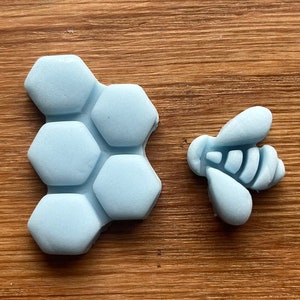 May include: A light blue honeycomb and a light blue bee, both made of silicone, are on a wooden surface.