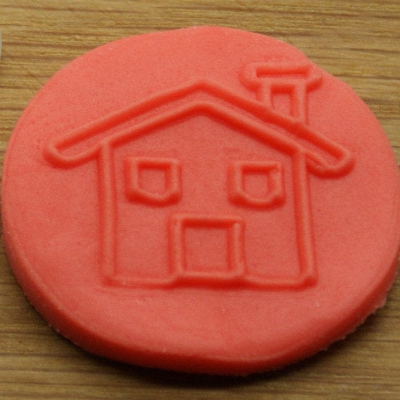 May include: A red rubber stamp with a house design. The house has a chimney, two windows, and a door.