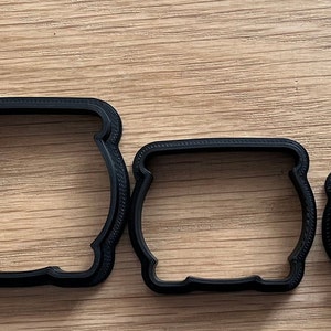 May include: Set of six black plastic cookie cutters shaped like cauldrons, arranged in order of size from largest to smallest.