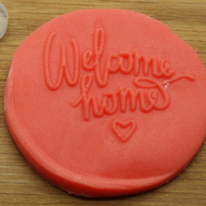 May include: Red round silicone stamp with the words "Welcome Home" and a small heart.