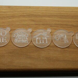 May include: Five clear plastic cookie cutters with different designs. The cutters are on a wooden surface. The designs include the words "Home", "Sweet Home", a house, a heart, and the words "Welcome Home".