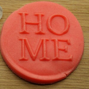 May include: A red, round, clay stamp with the word "HOME" embossed in white.