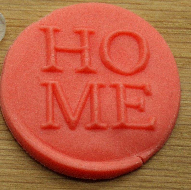 May include: A red, round, clay stamp with the word "HOME" embossed in white.