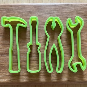 May include: Four green plastic cookie cutters shaped like tools: a hammer, a screwdriver, pliers, and a wrench.