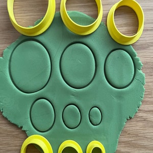 May include: A set of yellow plastic cookie cutters in various sizes, used to cut out circles in green dough.