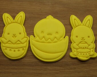 May include: Three yellow cookie cutters shaped like Easter bunnies holding eggs. The cutters are made of plastic and have a smooth, glossy finish.