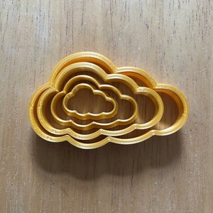 May include: A set of four gold-coloured metal cookie cutters shaped like clouds. The cutters are nested inside each other, with the smallest cutter in the centre.