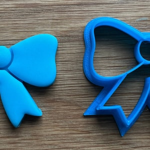 May include: A blue plastic cookie cutter shaped like a bow. The cutter is designed to cut out bow shapes from cookie dough.