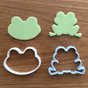 May include: Four cookie cutters in the shape of frogs. Two are green and two are white. The green frog cookie cutters are solid, while the white frog cookie cutters are hollow.