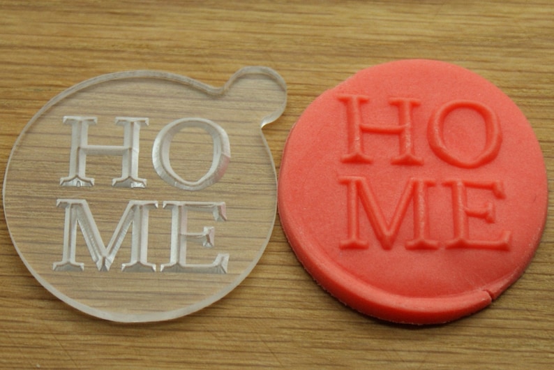 May include: A clear plastic cookie cutter and a red cookie with the word "HOME" embossed on it.