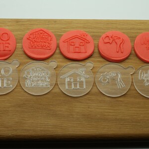 May include: Set of 10 clear and red plastic cookie cutters with various home-themed designs, including "Home", "Home Sweet Home", a house, a welcome sign, and a deer.