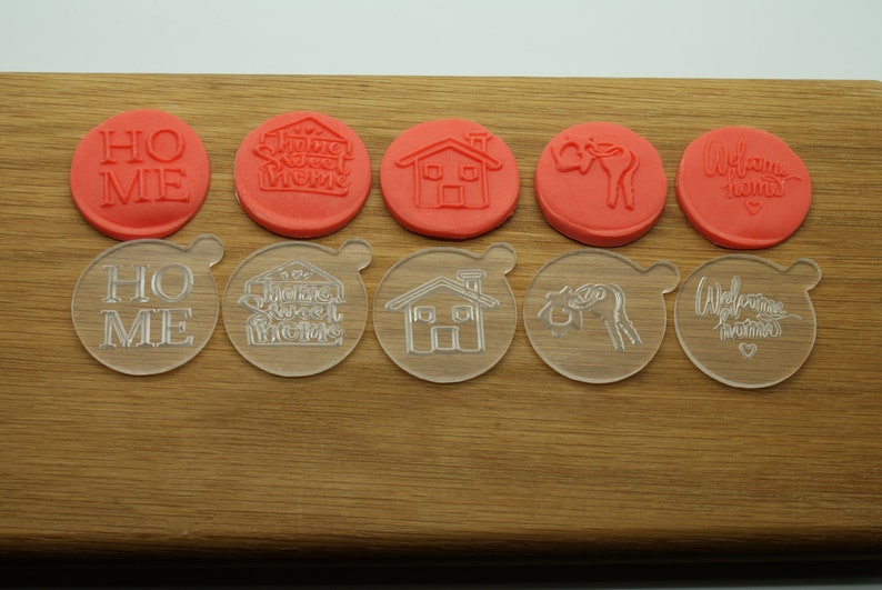 May include: Set of 10 clear and red plastic cookie cutters with various home-themed designs, including "Home", "Home Sweet Home", a house, a welcome sign, and a deer.