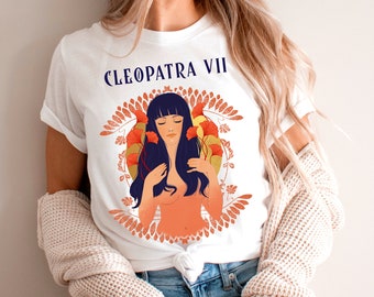May include: White t-shirt with a graphic of a woman with long dark hair and a floral design. The text "CLEOPATRA VII" is printed on the shirt.