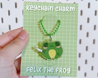 May include: Green frog keychain charm with a silver chain. The charm is on a green card with the text "keychain charm" and "Felix the Frog".