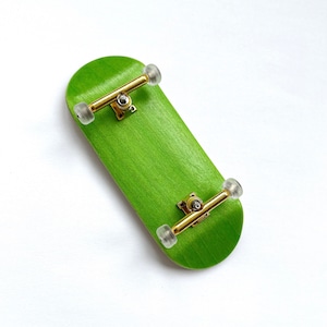 May include: A green fingerboard with gold trucks and clear wheels. The fingerboard is made of wood and has a smooth finish.