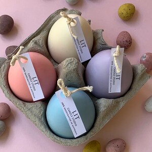 May include: Four pastel coloured egg-shaped candles in a cardboard egg carton. The candles are labelled "LIT Candle Studio 100% Handcrafted in Australia".