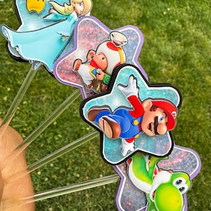 Puede incluir: Un conjunto de cuatro adornos decorativos con los personajes de Nintendo Rosalina, Toad, Mario y Yoshi. Cada personaje est&aacute; montado sobre un recorte en forma de estrella con acabado hologr&aacute;fico, unido a un palito de pl&aacute;stico transparente.