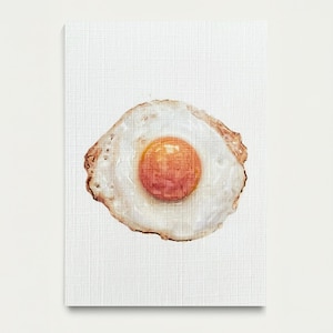 May include: A canvas print featuring a watercolor painting of a fried egg. The egg has a bright orange yolk and a white egg white with slightly browned edges. The background is a textured white.
