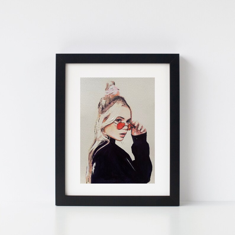 May include: A framed print of a painting depicting a woman with blonde hair wearing red heart-shaped sunglasses and a black turtleneck sweater. The woman is looking to the side and has a pink hair tie in her hair.