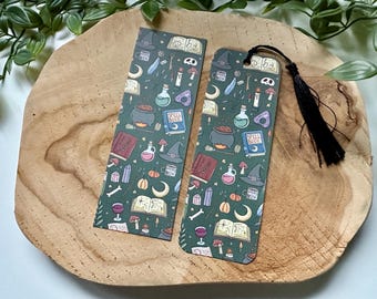 May include: Two green bookmarks with a black and white illustration of potion bottles, cauldrons, and other witchy items. The bookmark on the right has a black tassel.