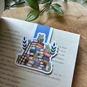 Può includere: Un adesivo con una pila di libri su cui salgono delle rane. L'adesivo è su un libro con il testo "A swirl of competing" e "Under any other circumstance."