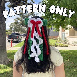 May include: A crochet hair accessory featuring a green headband base with a central white bow and long, cascading red and white crocheted ribbons. The text PATTERN ONLY is displayed in white letters at the top of the image.
