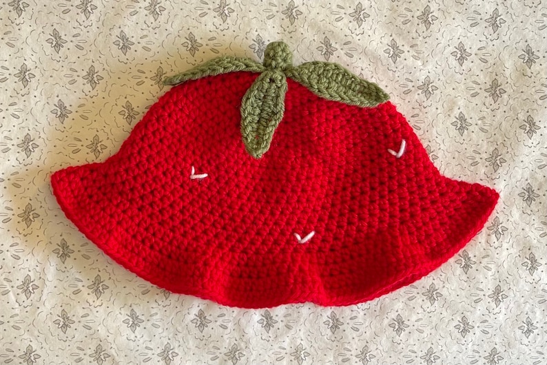 May include: Red crocheted bucket hat with green crocheted leaves on top and white crocheted details.