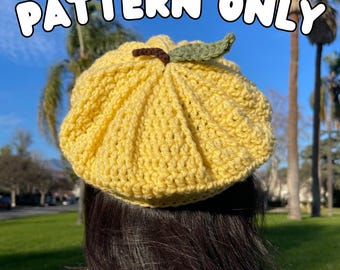 Puede incluir: Un gorro de punto amarillo con un detalle de hoja verde en la parte superior. El gorro lo lleva una persona con el pelo largo y oscuro.