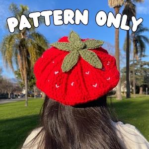 Puede incluir: Un gorro de fresa de punto de ganchillo rojo con hojas verdes y puntadas blancas. El gorro lo lleva una persona con el pelo largo y oscuro. El texto "PATTERN ONLY" se muestra encima del gorro.