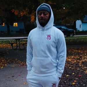 May include: A white hoodie with a red and white logo on the front and a matching white sweatpant with the same logo on the left leg. The hoodie has a drawstring hood and a kangaroo pocket.