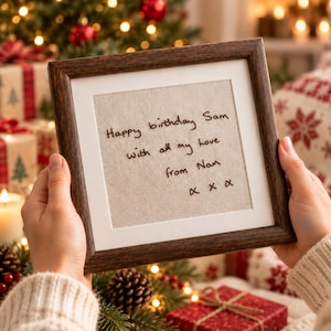 Könnte beinhalten: Ein quadratischer Holzrahmen mit dunkelbraunem Finish und einem hellbeigen Stoffeinsatz. Auf dem Stoff befindet sich ein schwarzer Sticktext mit dem Inhalt: Happy birthday Sam with all my love from Nan x x x.
