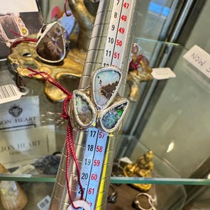 May include: A silver ring featuring three irregular, multi-colored opal stones set on a metal ring mandrel. The mandrel displays numerical sizing markings, with the ring positioned near the 17 mark on the scale, indicating a size 8 US ring size.
