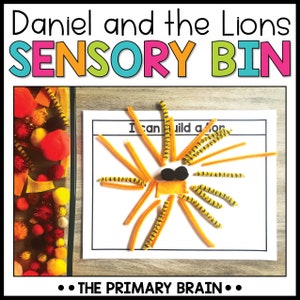 May include: A sensory bin activity for children featuring a craft project to build a lion using orange and black pipe cleaners. The text on the white card reads "I can build a lion".