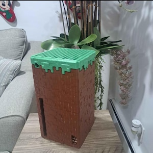 May include: A brown and green plastic toy building block set. The set is shaped like a tower with a green grass top.