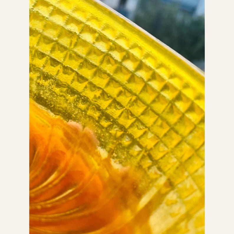 Second macro of the same edge, the lattice squares and tiny glitter flecks suspended in the cast resin visible against soft daylight.