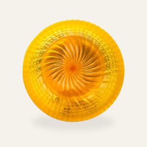 Yellow resin shaving bowl on a warm off-white background, the fan shaped swirl in the floor ringed by the moulded diamond wall.