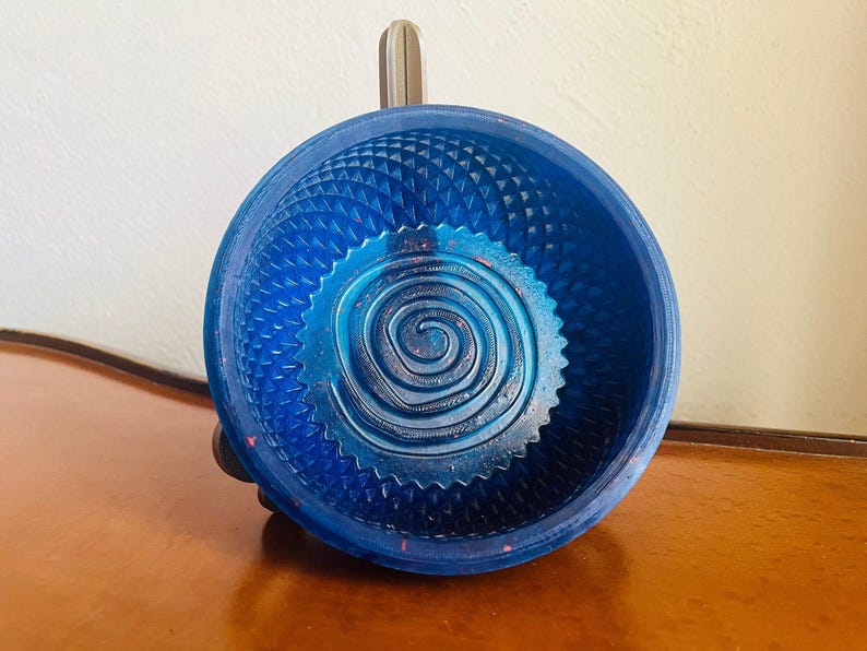 Royal blue sparkle resin shaving bowl standing upright on dark wood against a pale wall, the raised spiral coil visible in the floor and a moulded diamond lattice running around the wall.