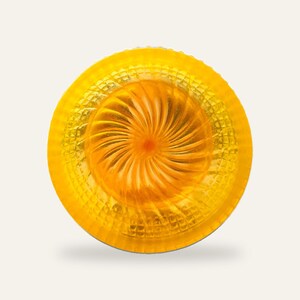 The yellow shaving bowl on a plain neutral background with no text, showing the full bowl shape and the orange fan swirl at its centre.