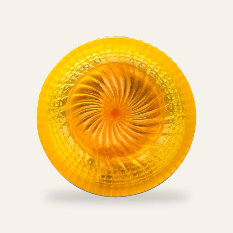 The yellow shaving bowl on a plain neutral background with no text, showing the full bowl shape and the orange fan swirl at its centre.