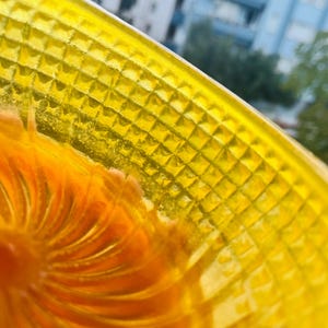 Close up of the yellow shaving bowl wall in daylight, showing the pyramid cut texture in cast resin and the orange fan swirl inside the lather well.