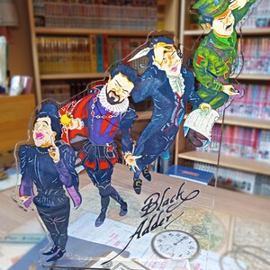 May include: A clear acrylic stand with four cartoon figures. The figures are dressed in colorful costumes and are holding various props. The stand features a clock and the text "Black Adder".