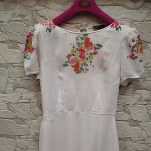 Könnte beinhalten: Ein weißes Kleid mit Blumenmuster. Das Kleid hat kurze Ärmel und einen runden Ausschnitt. Das Kleid ist aus einem leichten Stoff.