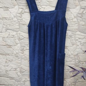 Może przedstawiać: Granatowa sukienka z frotte z szerokimi ramiączkami i kwadratowym dekoltem. Sukienka ma marszczony gorset i jedną kieszeń po prawej stronie. Sukienka wisi na białym wieszaku.