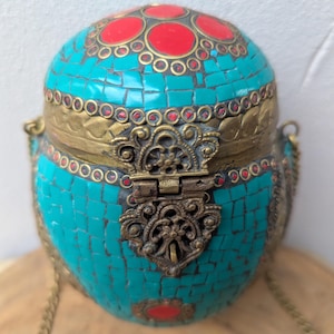 May include: A turquoise mosaic-tiled, spherical purse with brass accents and a decorative clasp. The top features red circular inlays. A delicate chain strap is attached. The purse is likely handmade and has an antique or vintage aesthetic.