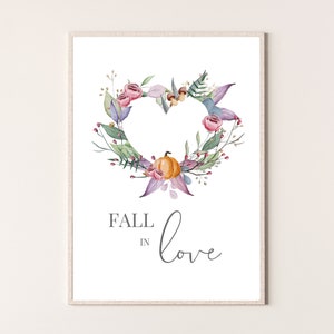 Może przedstawiać: Drukowana grafika artystyczna z akwarelową ilustracją wieńca w kształcie serca z jesiennych liści, kwiatów i dyni. Tekst "Fall in love" jest napisany pod wieńcem.