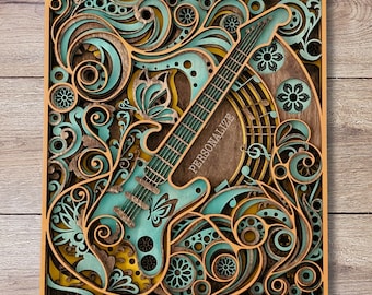 May include: A layered wooden art piece featuring a teal electric guitar with floral and musical note accents. The word "PERSONALIZE" is printed on the guitar. The artwork is framed in a light brown wooden border.