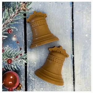 May include: Two brown ceramic bells with a decorative design on the top. The bells are on a wooden surface.