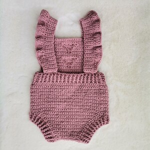 May include: A crocheted baby romper in a dusty rose color with ruffled straps.
