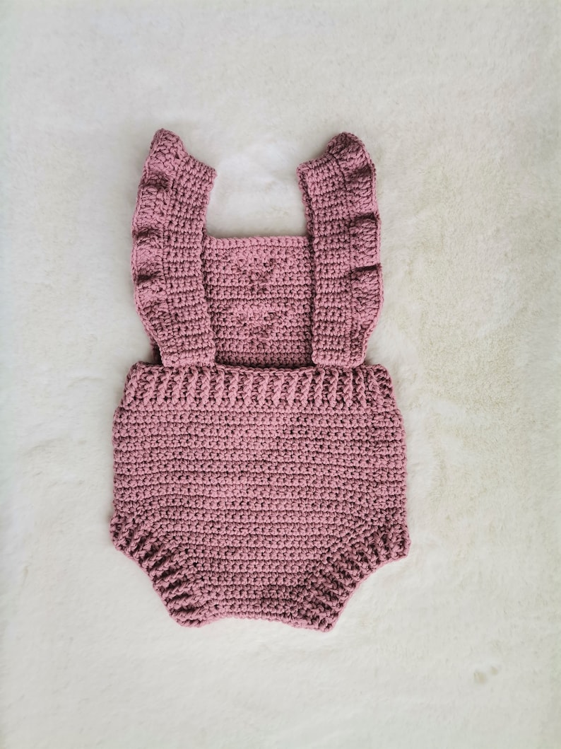 May include: A crocheted baby romper in a dusty rose color with ruffled straps.